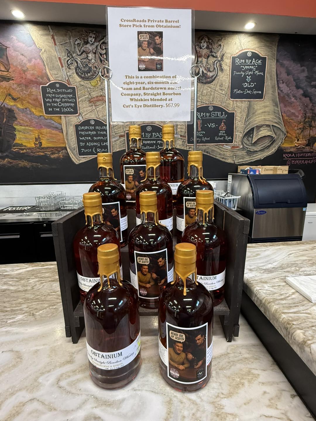 Display of Obtanium straight bourbon whiskey bottles with gold wax-dipped tops on a store counter beneath a sign for a CrossRoads private barrel pick.