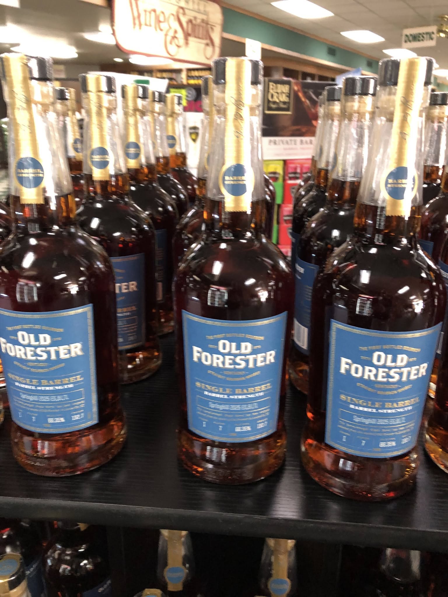 Rows of Old Forester Single Barrel bourbon bottles with blue labels and gold necks displayed on a liquor store shelf.