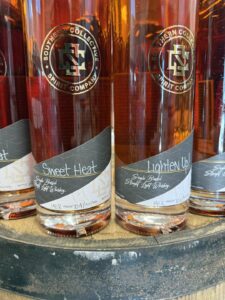 Close-up of Southern Collective Spirit Company whiskey bottles, showing amber liquid and labels “Sweet Heat” and “Lighten Up!” (single barrel straight light whiskey).