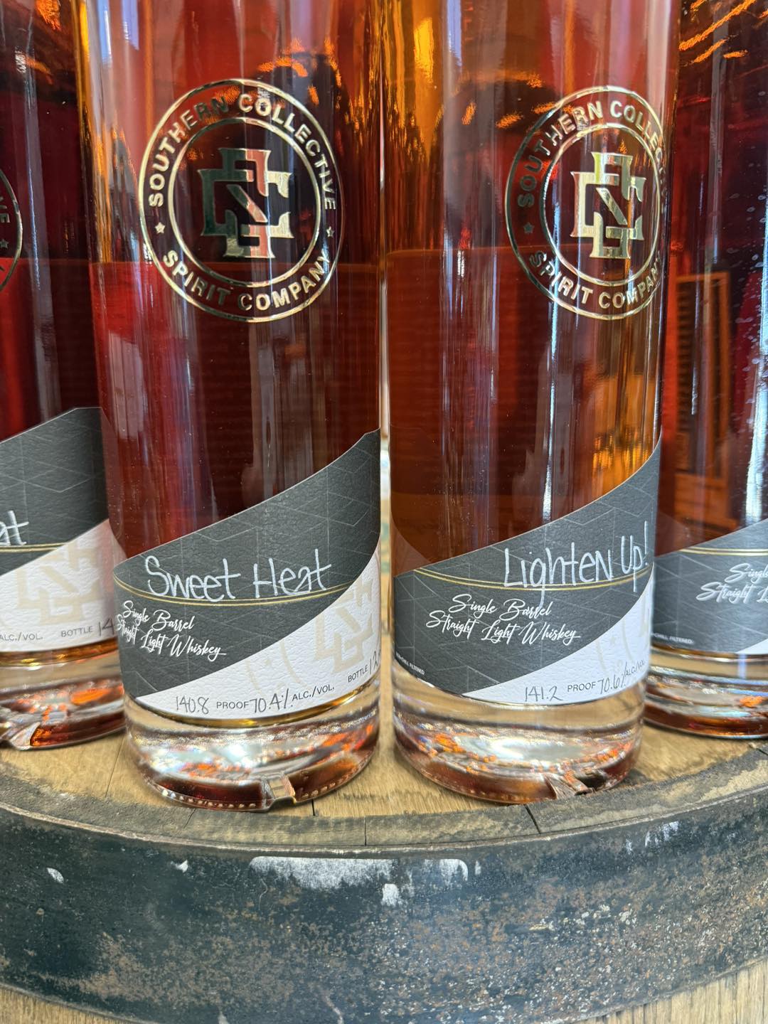 Close-up of Southern Collective Spirit Company whiskey bottles, showing amber liquid and labels “Sweet Heat” and “Lighten Up!” (single barrel straight light whiskey).