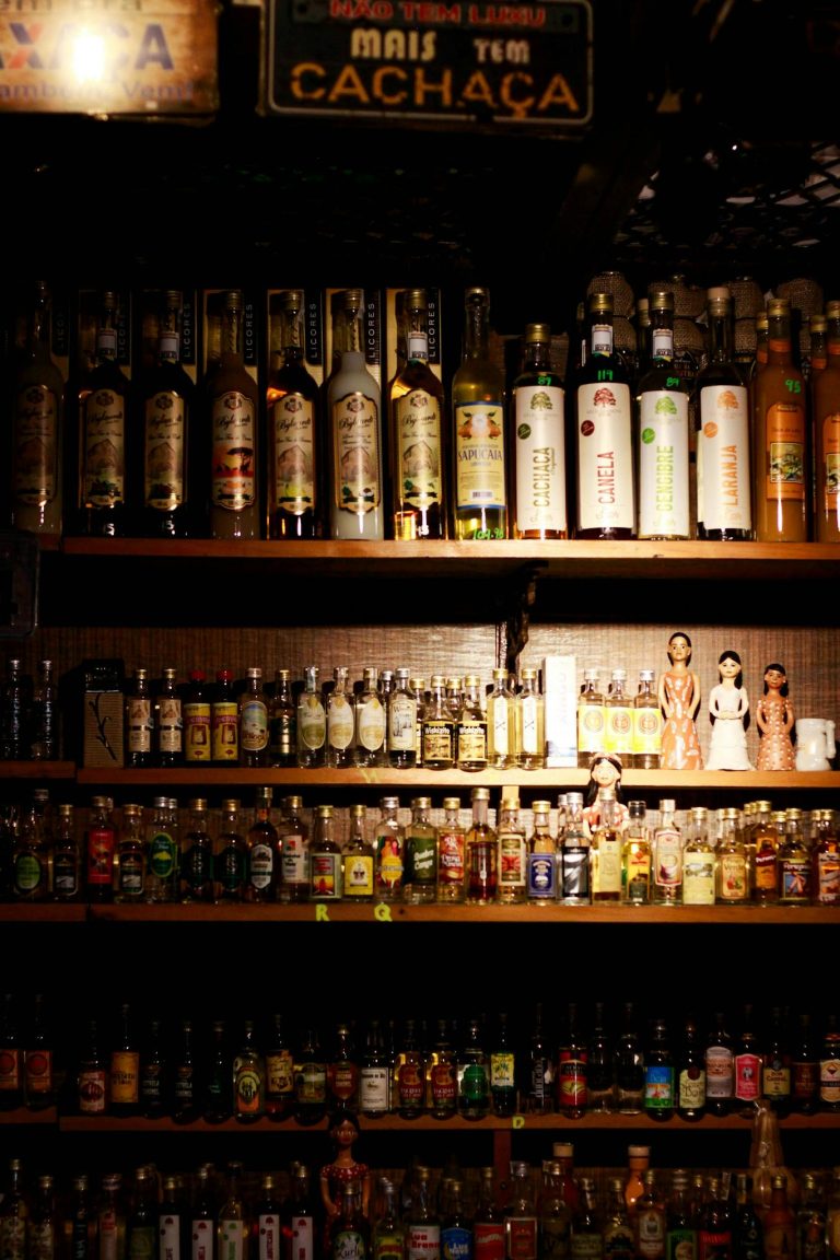 A variety of liquor bottles displayed on a bar's wooden shelf under warm lighting.