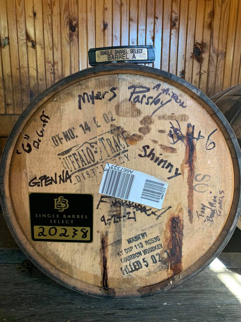 Front of a Buffalo Trace bourbon barrel (Single Barrel Select, Barrel A) with handwritten markings, barcode sticker, and an ID label reading “20278,” leaning against a wooden wall.