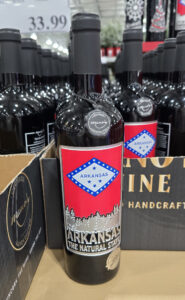 Close-up of an “Arkansas” handcrafted wine bottle with a red label reading “Arkansas, The Natural State,” displayed among similar bottles on a store shelf.