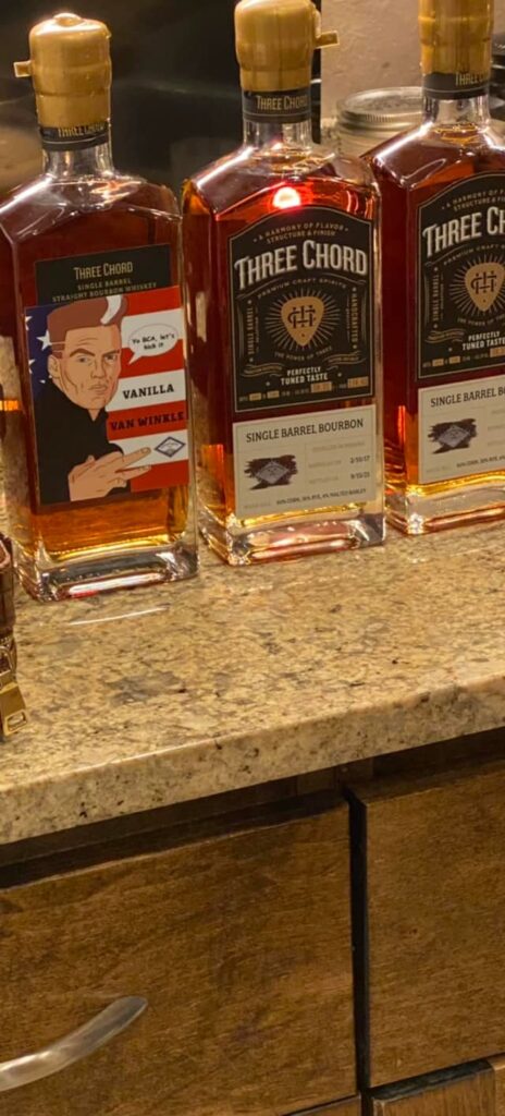 Three bottles of Three Chord Single Barrel Straight Bourbon Whiskey on a kitchen counter, including a Vanilla Van Winkle label and two Three Chord Single Barrel Bourbon bottles.