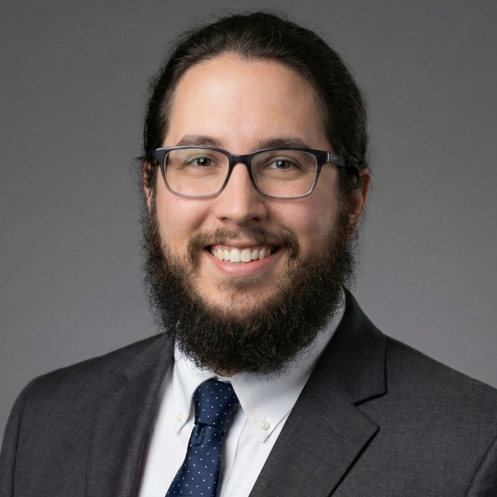 Professional headshot of David McMahon smiling, wearing a dark grey suit, blue tie, and glasses with a full beard against a solid grey background.