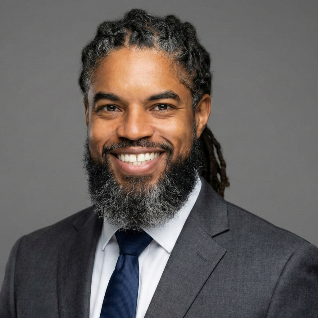 Professional headshot of David Shropshire smiling, wearing a dark grey business suit and navy tie, with dreadlocks and a full beard, against a neutral grey background.