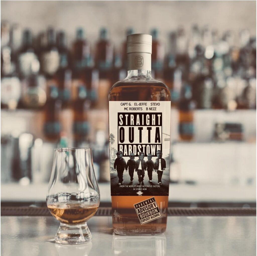 Close-up product photo of a bourbon whiskey bottle on a bar counter with a tulip-shaped tasting glass beside it. The bottle contains amber-colored bourbon and has a cream label styled like a music poster reading ‘STRAIGHT OUTTA BARDSTOWN,’ with small text at the top listing names (Capt G., El-Jeffe, Stevo, MC Roberts, B Nezz) and a black-and-white image of five men walking down a street. Near the bottom of the label is a ‘Parental Advisory’ graphic that reads ‘Bourbon Explicit Alcohol.’ In the softly blurred background, shelves are lined with multiple liquor bottles, suggesting a bourbon bar or whiskey tasting room setting.