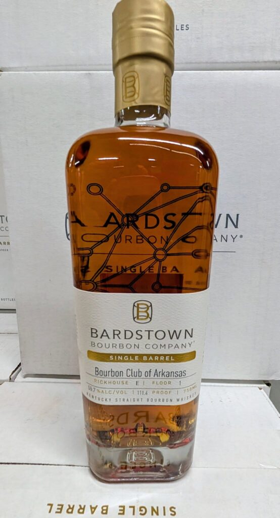 Front view of a Bardstown Bourbon Company Single Barrel Kentucky straight bourbon whiskey bottle with amber liquid, gold foil neck, and label reading ‘Bourbon Club of Arkansas,’ ‘Rickhouse E1, Floor 1,’ 55.7% ABV, 111.4 proof, 750 ml, photographed against stacked white Bardstown Bourbon Company boxes.