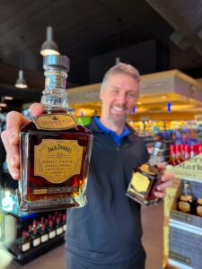 Man holding a Jack Daniel’s Single Barrel Barrel Proof Tennessee Whiskey bottle in a liquor store aisle, with shelves of spirits and wine in the background.
