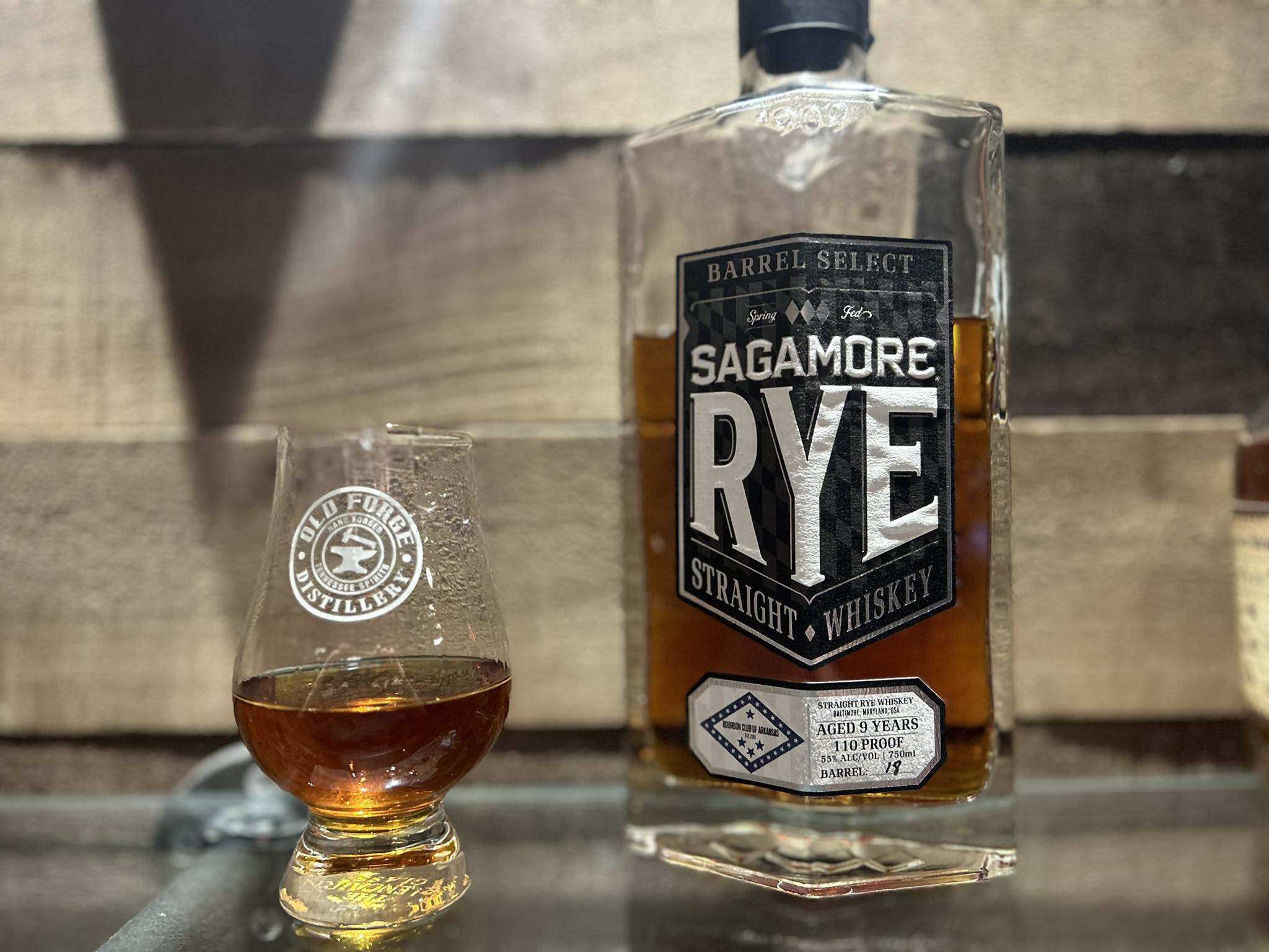 Sagamore Rye Barrel Select straight rye whiskey bottle (aged 9 years, 110 proof) beside a whiskey tasting glass holding a small pour of amber rye whiskey.